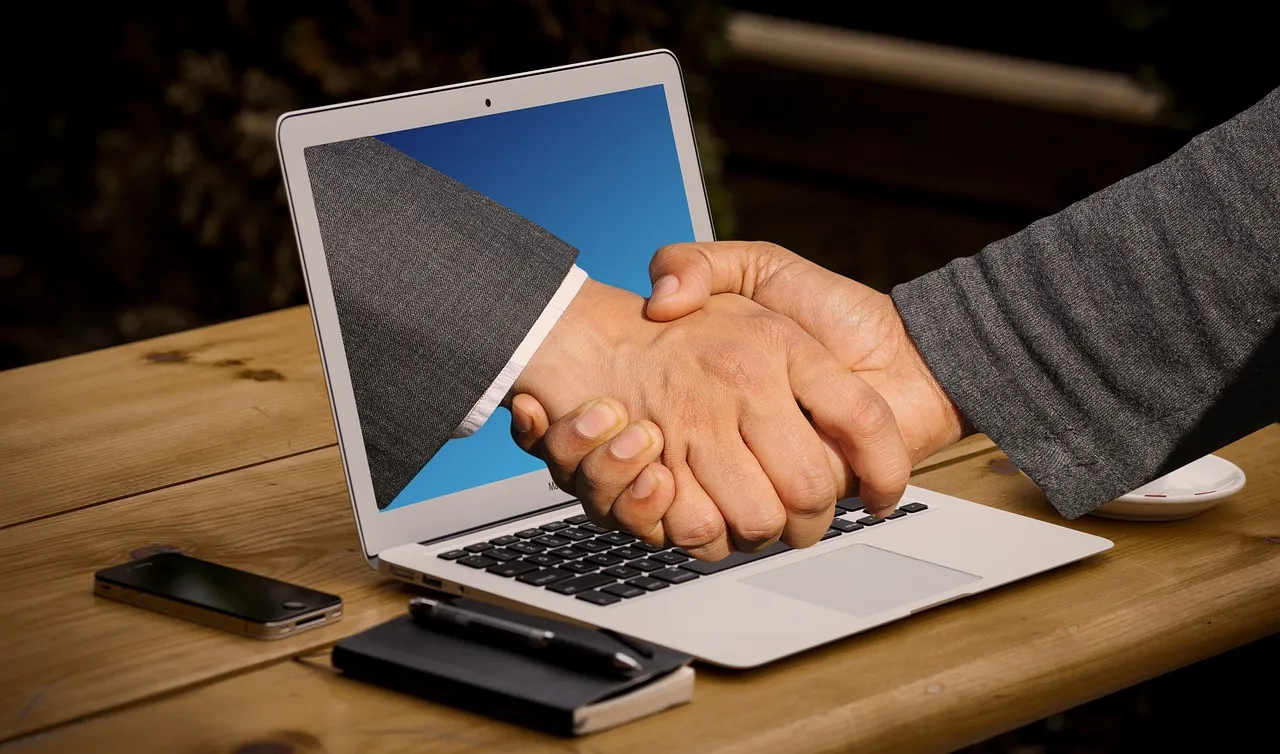 Photo showing handshake, hands, laptop and monitor.