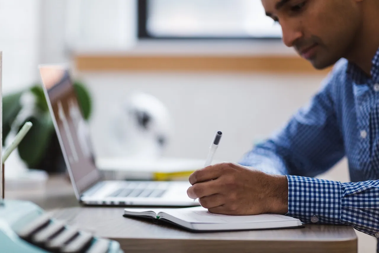 Photo showing man, writing, laptop and computer.